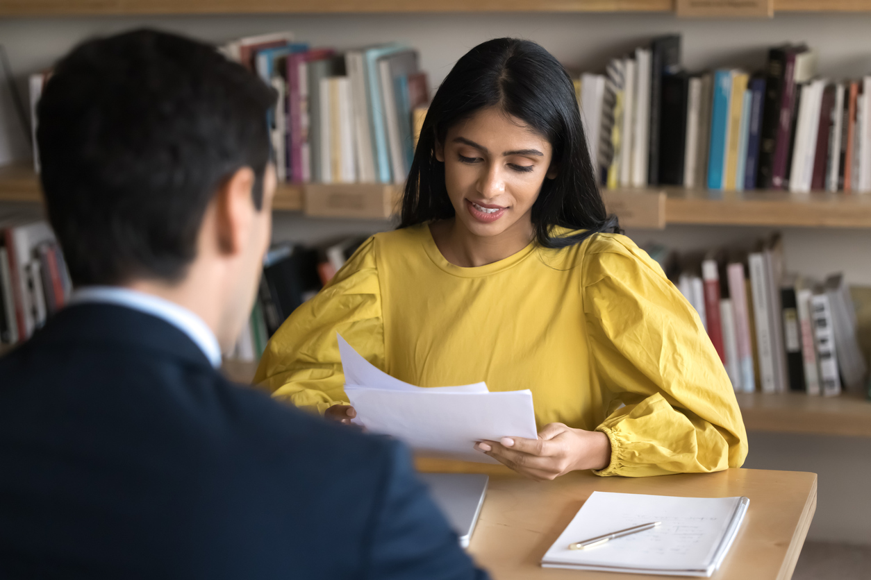 An adult reviews paperwork with a pupil at a table in a school library.